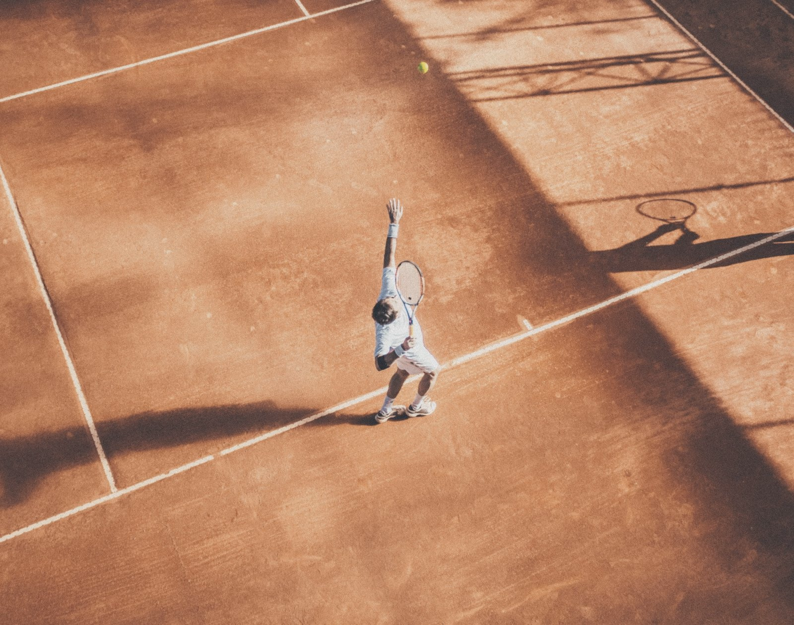A tennis player serving on a clay court, seen from above